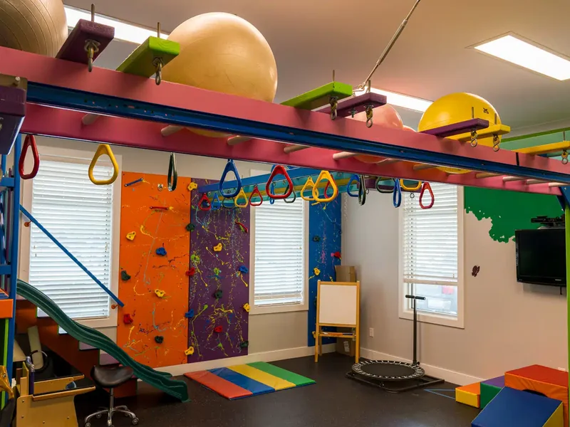 Wide view of the sensory gym with a climbing wall, monkey bars and hanging exercise balls