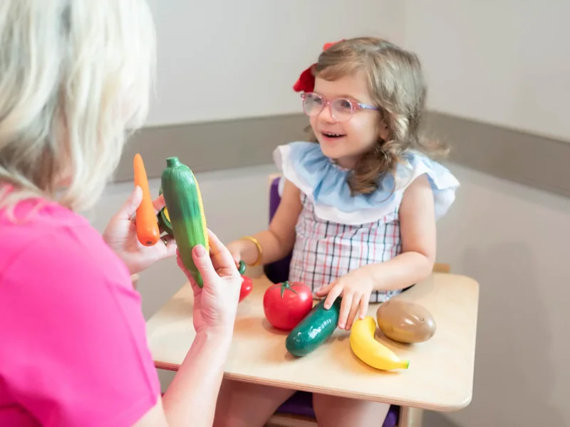 Therapist and a young child naming play food together at a small table
